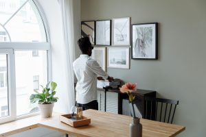 A man arranges framed prints on a wall, enhancing the modern decor of a bright home interior.