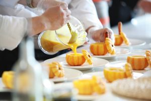 Chef performing culinary artistry by pouring vibrant pumpkin soup in decorative pumpkins.